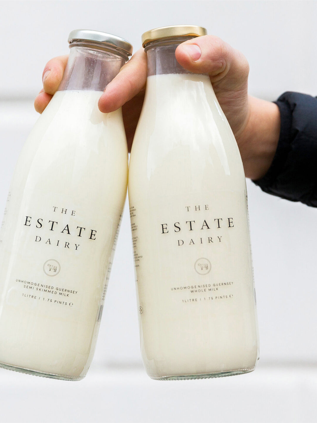Hand holding two bottles of The Estate Dairy milk.