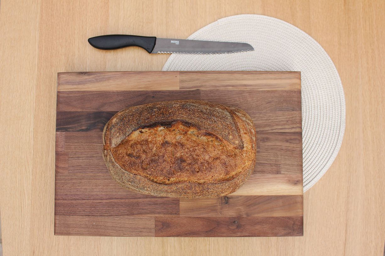 Image of fresh Butter & Crust sourdough loaf on a wooden chopping board, next to a white plate and bread knife