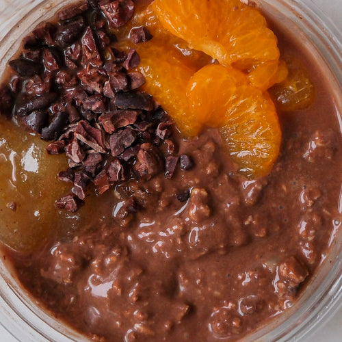 Close up , no lid, of dark chocolate, bitter orange marmalade, mandarins, cacao nibs, and coconut yoghurt overnight oats bowl.