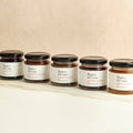 Six assorted jars of Butter & Crust jam on a beige background.
