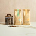 Two Monmouth Coffee Company bags and a jar of coffee beans on a marble surface with a beige background.