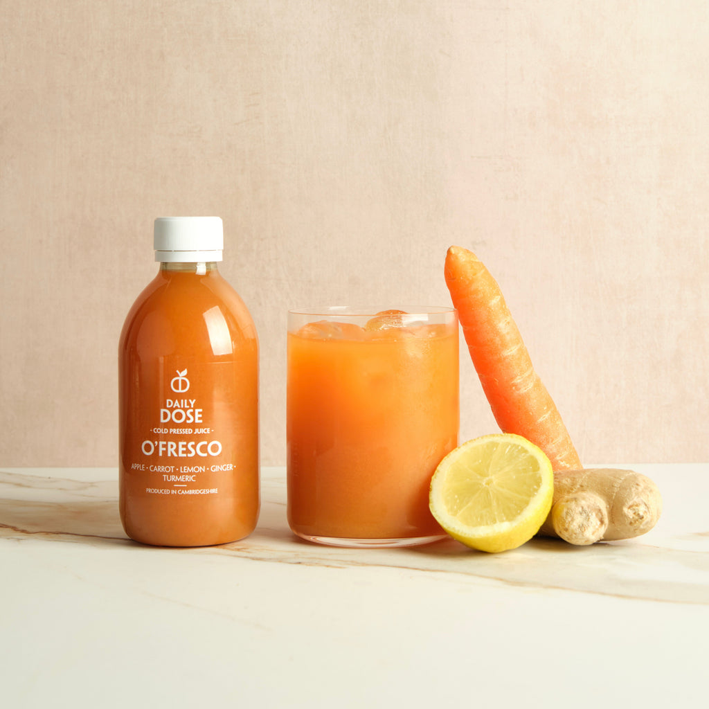 Bottle and glass of 'Daily Dose O'Tresco' juice with carrot, lemon, and ginger on a marble surface with a beige background.
