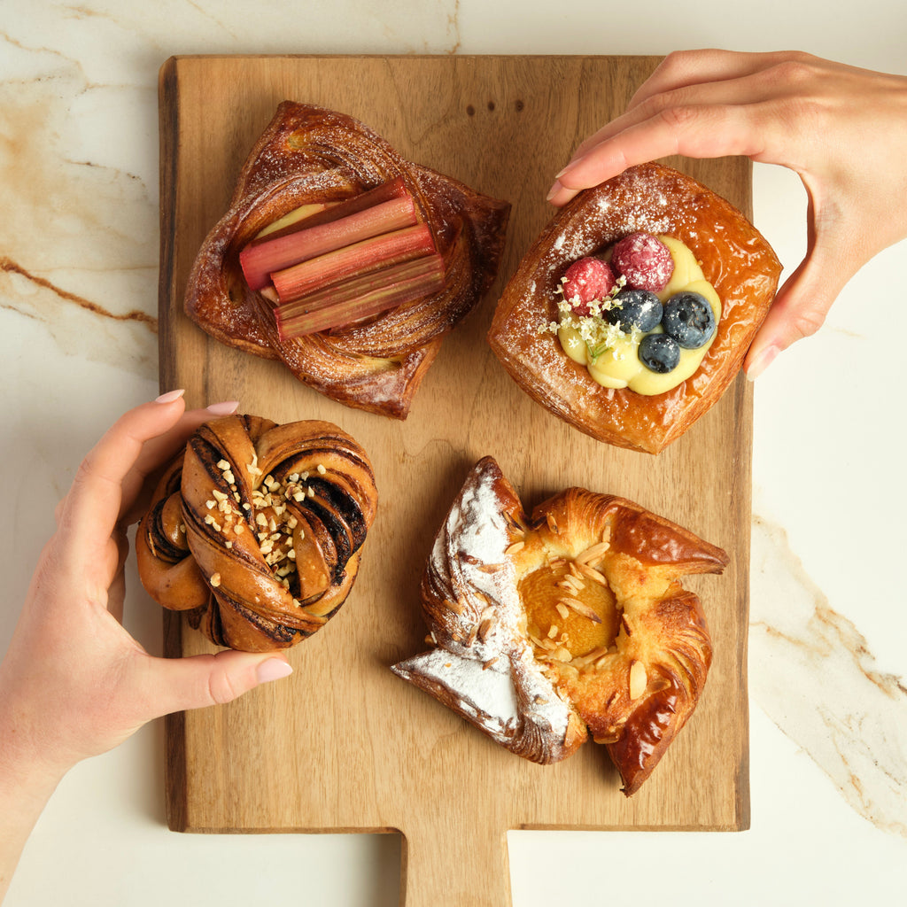 Four assorted pastries on a wooden cutting board on top of a marble surface.