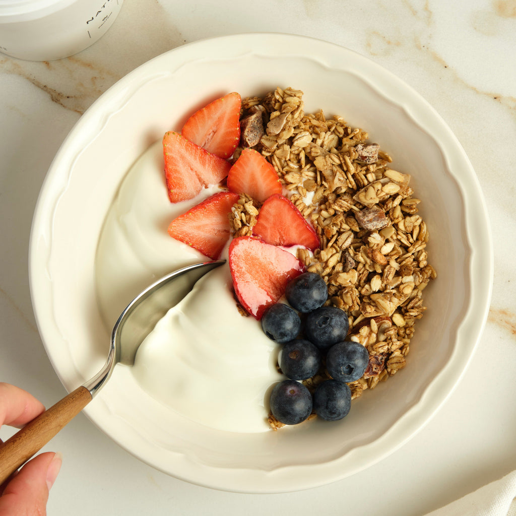 Yogurt bowl with granola and berries on a marble surface.
