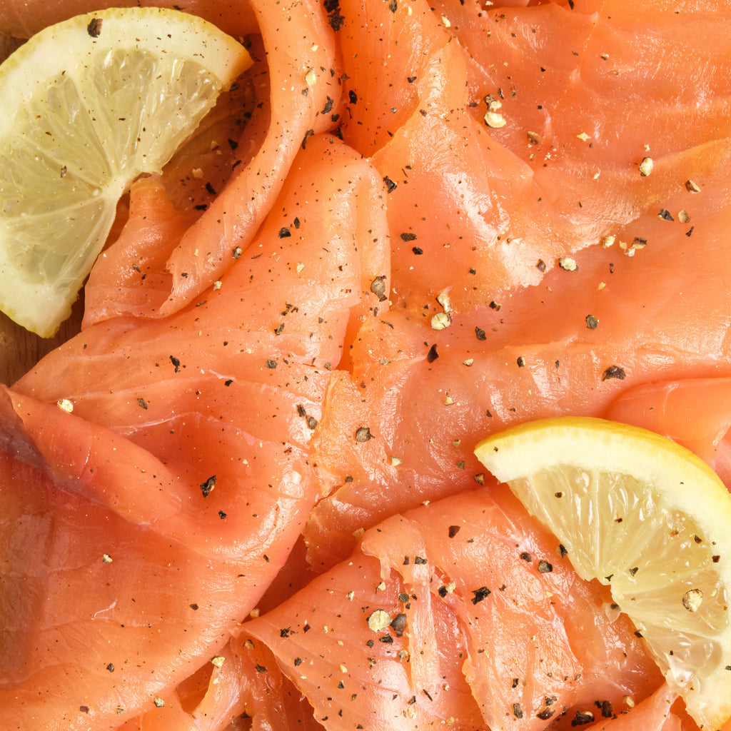Close up of raw salmon topped with pepper flakes and lemon.