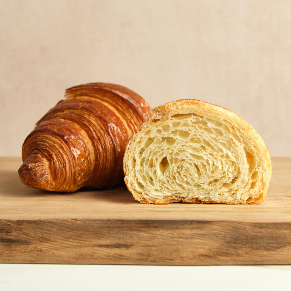 Croissant sliced in half on a wooden surface against a beige background.