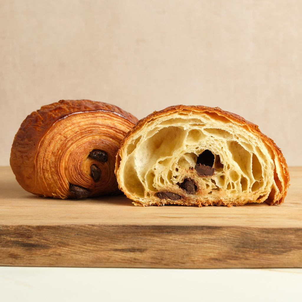 Croissant sliced open showing chocolate filling on a wooden surface against a beige background.