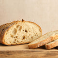 Loaf of bread with slices on a wooden cutting board against a beige background.