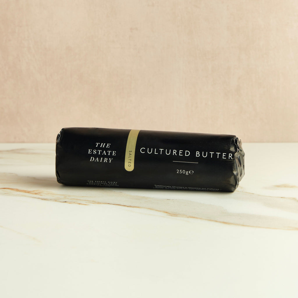 Roll of salted cultured butter from The Estate Dairy on a marble surface with a beige background.