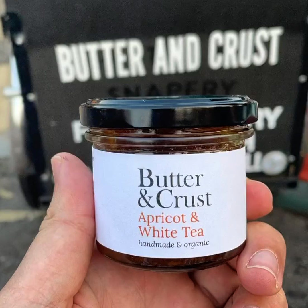 Hand holding a small jar of Butter & Crust's Apricot & White Tea handmade/organic preserves.