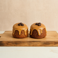 Two small round coffee cakes with caramel glaze and chocolate chips on a wooden board against a beige background