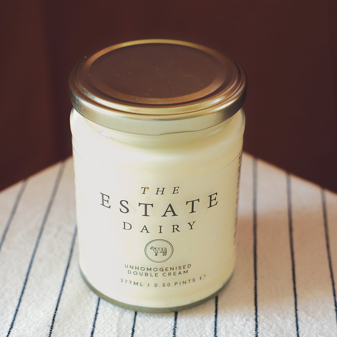 Jar of cream from The Estate Dairy on a striped cloth.